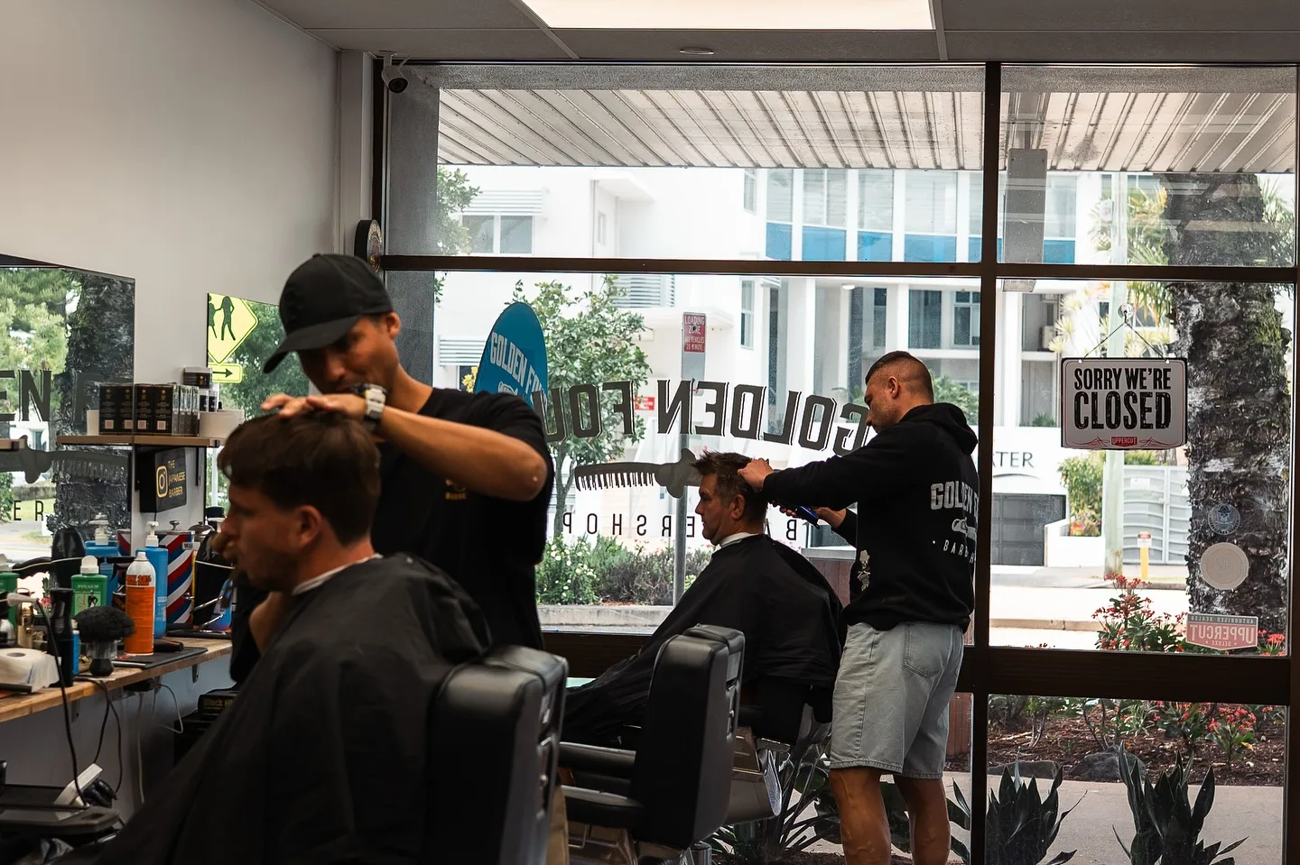 Two Golden Four barbers working on adult clients inside the shop
